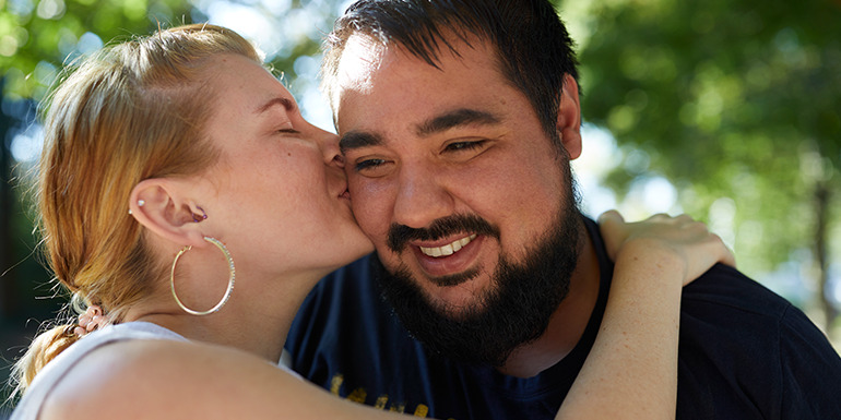 Zwei Personen in einer vertrauten Umarmung im Freien an einem sonnigen Tag.